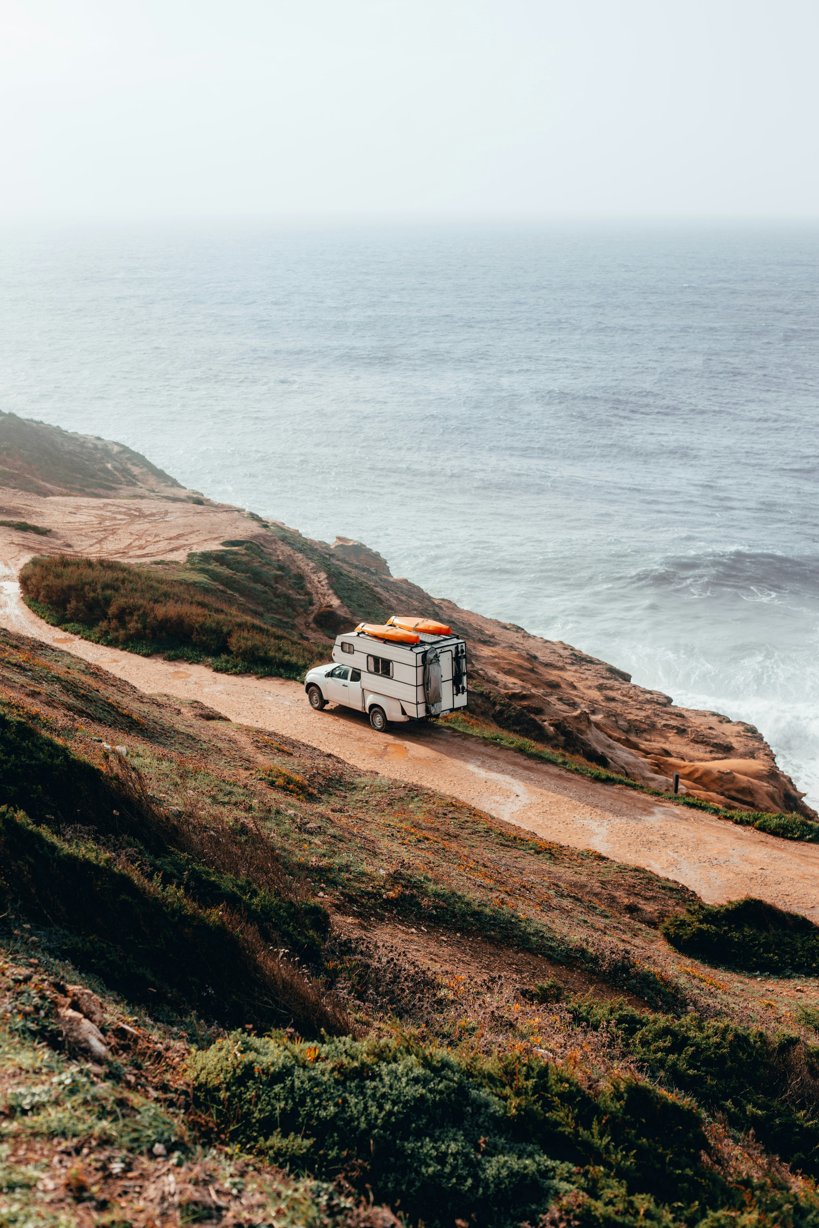 A white camper truck parked on a dirt path along the rugged cliffs of Tasmania’s east coast, with fog rolling in over the ocean